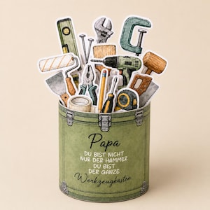 May include: A green toolbox-shaped card filled with various tools, including a level, wrench, drill, and saw. The card has the word "Papa" and German text on the front.