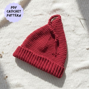 May include: A handmade, red crochet hat with a braided cord and tassel detail. The hat features a ribbed brim and a pointed top. The image includes text that reads "PDF Crochet Pattern" in a light purple circle.
