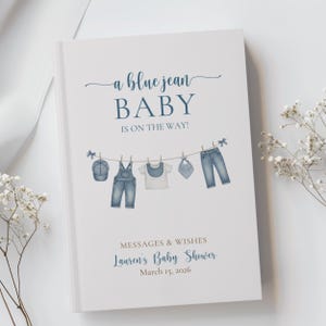 May include: A white baby shower guest book with the text "a blue jean BABY IS ON THE WAY!" in blue script. The cover features illustrations of baby clothes hanging on a clothesline, including a hat, overalls, a shirt, a bib, and jeans. The text "MESSAGES & WISHES" and "Lauren's Baby Shower March 15, 2026" are also included.