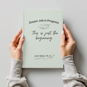 May include: A light green book with the text "Dream Job in Progress" and "...This is just the beginning" in black script. The author's name, Josh Wells, Ph. D., is also printed on the book. The book is held by two hands.