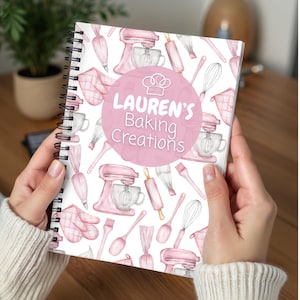 May include: A spiral-bound notebook with a pink and white baking-themed design. The cover features the text "Lauren's Baking Creations" in a pink circle, surrounded by illustrations of kitchen tools like mixers, whisks, and rolling pins.