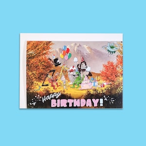 May include: A colorful birthday card featuring cartoon characters celebrating with balloons, cake, and gifts. The card says "Happy Birthday!" in pink letters.