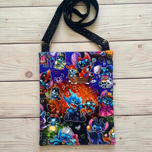 Puede incluir: Un bolso bandolera rectangular con una correa negra con lunares blancos. La tela del bolso est&aacute; estampada con personajes de dibujos animados coloridos sobre un fondo oscuro. El bolso tiene herrajes met&aacute;licos dorados.