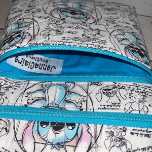 May include: A quilted pouch featuring a white background with a repeating blue and pink character print and black cursive text. The pouch has a bright blue interior lining, a matching blue zip, and a white label reading jennaclaire boutique.