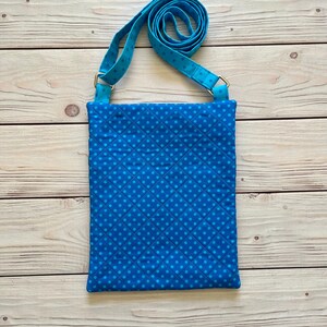 May include: A blue crossbody bag with a repeating dot pattern and a matching adjustable strap. The bag is rectangular with a quilted design. The strap is attached with silver-colored metal hardware.