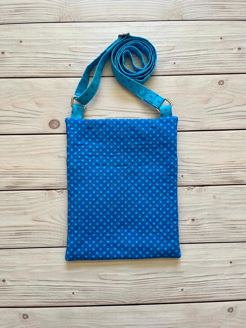 May include: A blue crossbody bag with a repeating dot pattern and a matching adjustable strap. The bag is rectangular with a quilted design. The strap is attached with silver-colored metal hardware.