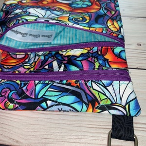 May include: A quilted fabric pouch featuring a colorful, stained-glass style print of Jack Skellington. The pouch has two purple zippered compartments and a light blue striped interior lining with a white label reading Jenna Claire Boutique.