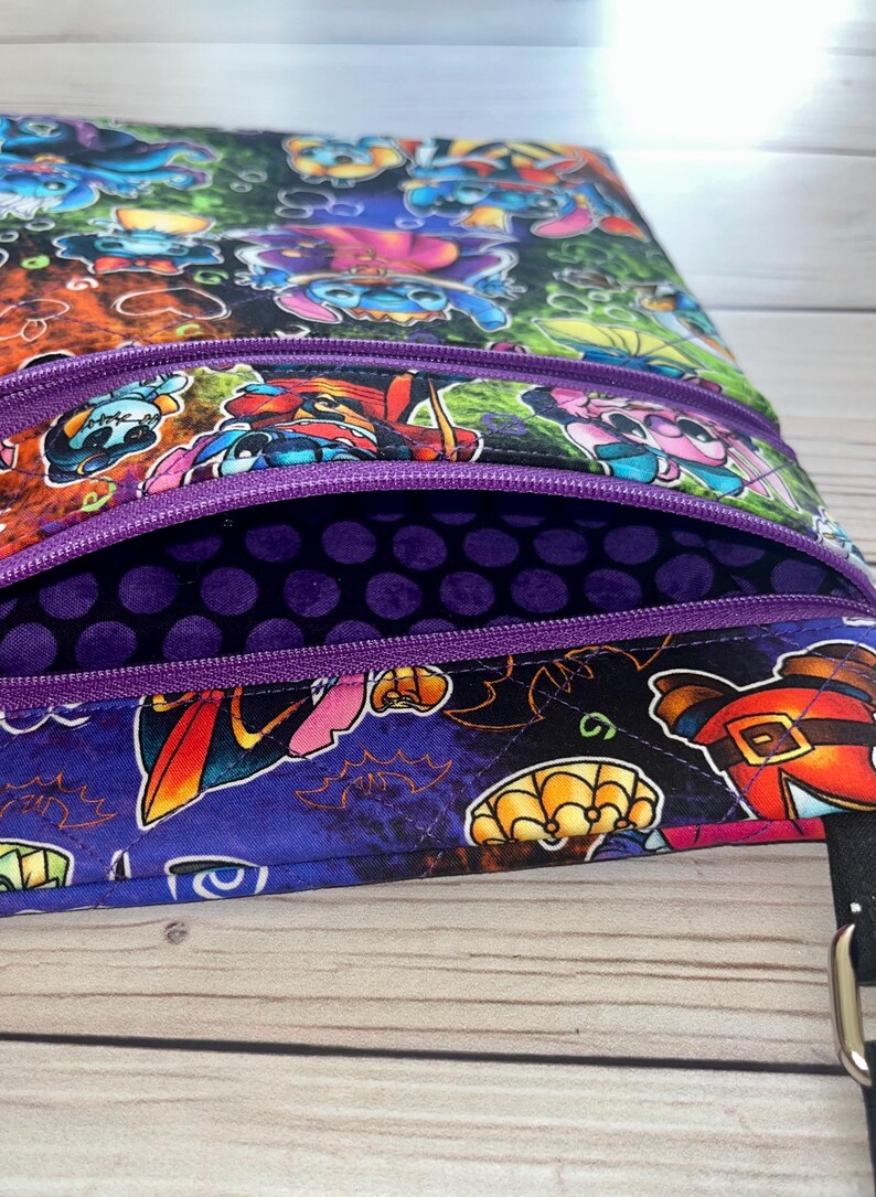 Puede incluir: Bolso bandolera multicolor con m&uacute;ltiples compartimentos con cremallera. El bolso presenta un estampado vibrante de personajes de dibujos animados con disfraces de Halloween. El interior es morado oscuro con lunares y las cremalleras son moradas.