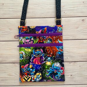 Puede incluir: Bolso bandolera rectangular con estampado de personajes de dibujos animados coloridos. El bolso tiene una correa negra con lunares blancos, tres compartimentos con cremallera morada y herrajes dorados. El estampado incluye varios personajes con disfraces.