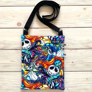 May include: A quilted crossbody bag featuring a vibrant, stained-glass style print of characters from The Nightmare Before Christmas, including Jack Skellington and Sally. The bag has a black adjustable strap and a rectangular, stitched fabric body.