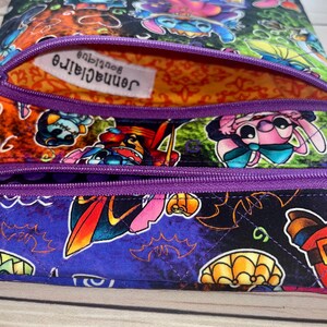 Puede incluir: Una colorida bolsa con cremallera con estampado de personajes de dibujos animados. La bolsa presenta una cremallera morada y un interior estampado. La tela exterior muestra varios personajes de dibujos animados en una vibrante paleta de colores. El forro interior es naranja con un patr&oacute;n decorativo.