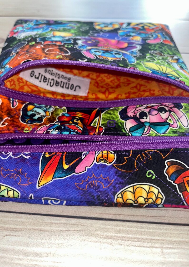 Puede incluir: Una colorida bolsa con cremallera con estampado de personajes de dibujos animados. La bolsa presenta una cremallera morada y un interior estampado. La tela exterior muestra varios personajes de dibujos animados en una vibrante paleta de colores. El forro interior es naranja con un patr&oacute;n decorativo.