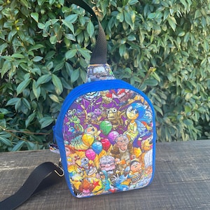 May include: A blue and black crossbody bag with a colorful print of various cartoon characters from popular animated movies. The print includes characters like Buzz Lightyear, Woody, Mike Wazowski, Sulley, and more.