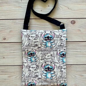 May include: A rectangular crossbody bag featuring a light-coloured fabric with a repeating print of the blue character Stitch from Lilo & Stitch, surrounded by scientific sketches, diagrams, and text including the word Warning.