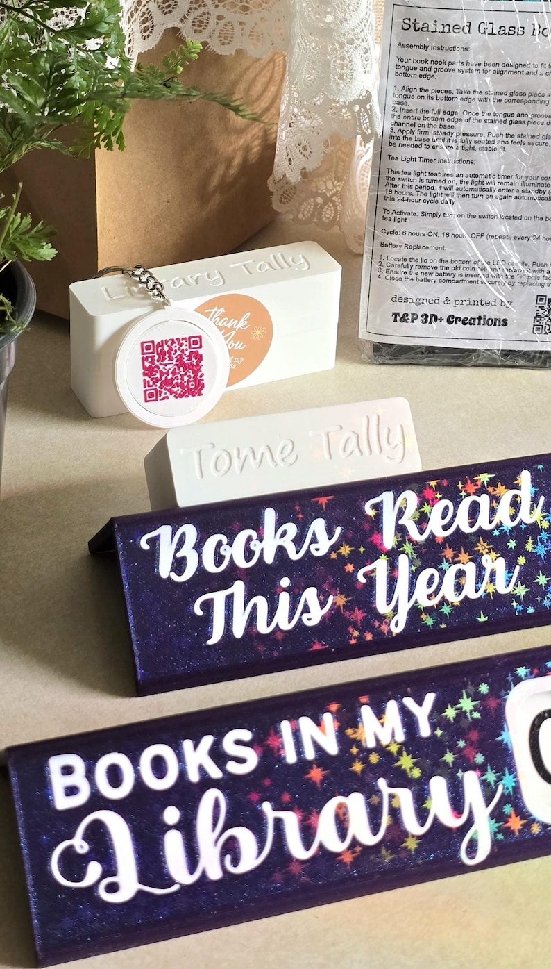 May include: A collection of book-themed decor items. Includes a white rectangular block with "ary Tally" and a QR code tag, a "Tome Tally" block, and two dark blue bookends with the text "Books Read This Year" and "Books In My Library".