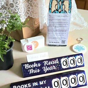 May include: An assortment of reading-themed items, including a stained glass book nook, a keychain with "Sweet Dreams", and two "Books Read This Year" and "Books in My Library" counters. The counters have white numbers and a starry background.