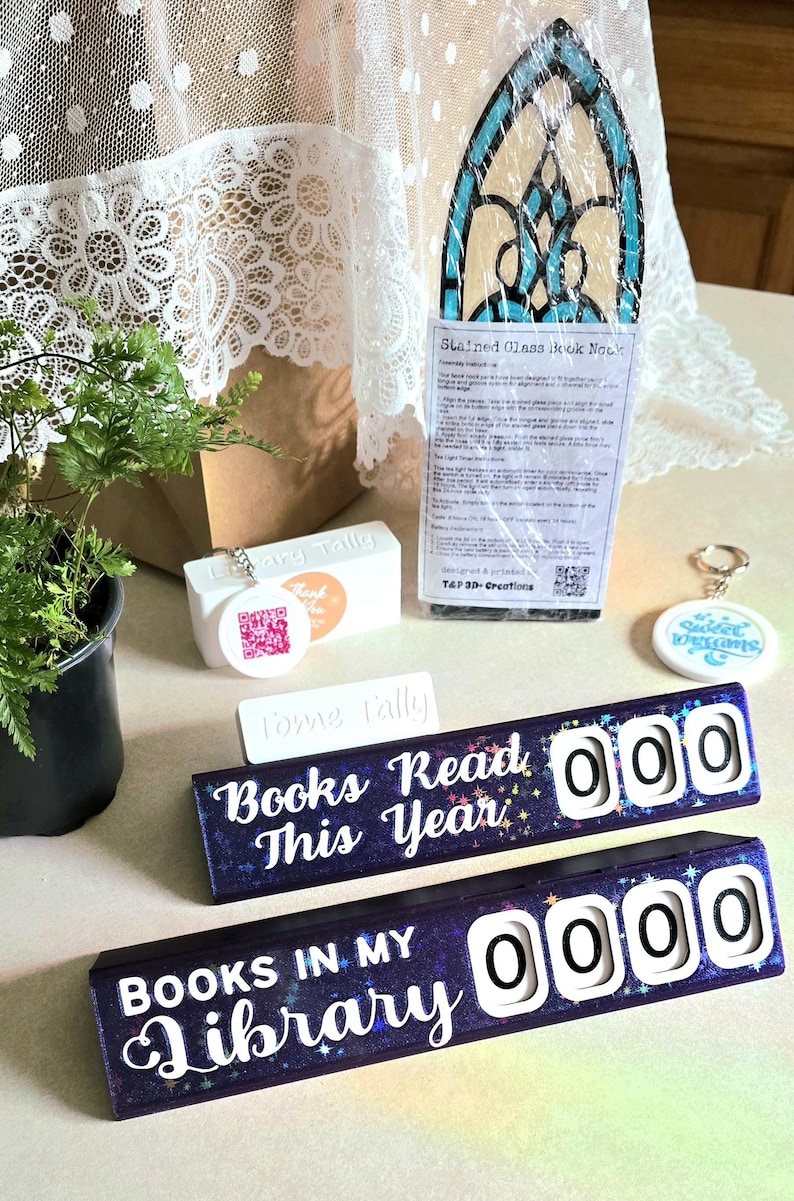 May include: An assortment of reading-themed items, including a stained glass book nook, a keychain with "Sweet Dreams", and two "Books Read This Year" and "Books in My Library" counters. The counters have white numbers and a starry background.