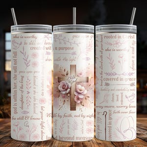 Op de afbeelding: Drie roestvrijstalen bekers met deksels en rietjes. De bekers hebben een bloemen- en kruisontwerp met inspirerende tekst in roze. De middelste beker heeft de woorden "Child of God".