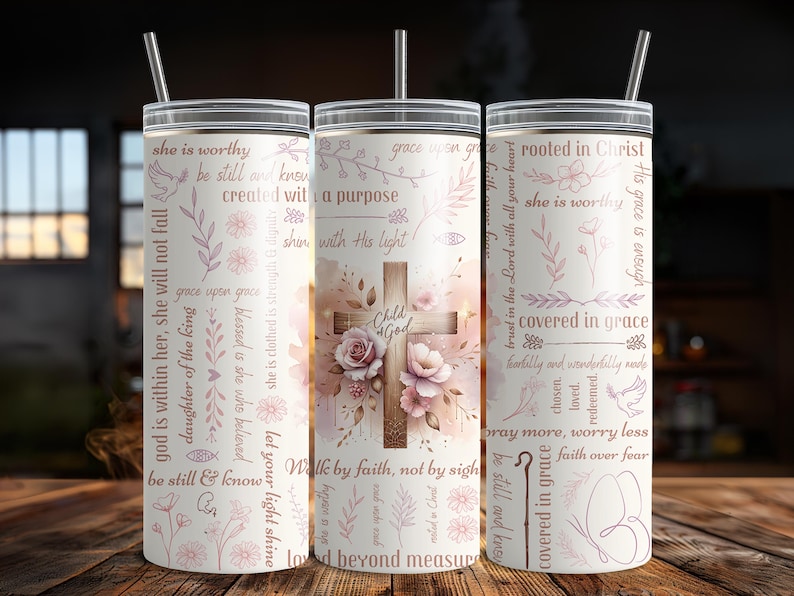 Op de afbeelding: Drie roestvrijstalen bekers met deksels en rietjes. De bekers hebben een bloemen- en kruisontwerp met inspirerende tekst in roze. De middelste beker heeft de woorden "Child of God".