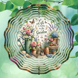 Può includere: Un mulinello da giardino in metallo con sfondo bianco e design floreale colorato. Il testo "Life is better in the Garden" è stampato sul mulinello.