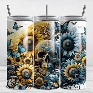 May include: Three stainless steel tumblers with a white background and a design of a skull surrounded by sunflowers and butterflies. The skull has a blue and gold design and the sunflowers have blue and yellow petals.