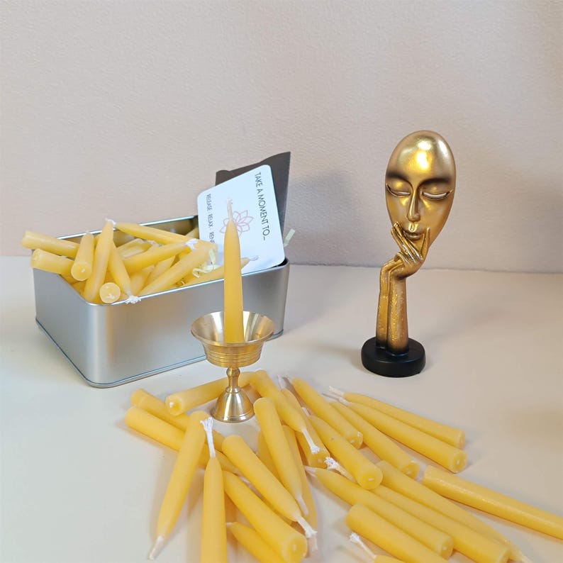 May include: A tin box filled with small, yellow beeswax candles. A single candle is lit in a brass candlestick. The text on the card reads "Take a moment to - Relax, Breathe, Trust".