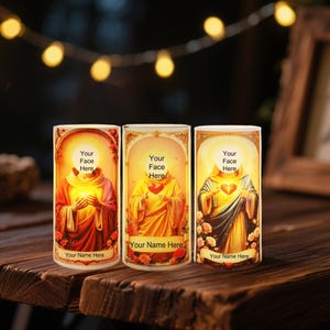 Könnte beinhalten: Drei dekorative Kerzenhalter mit religiösen Bildern. Jeder zeigt eine heilige Figur mit einem Herzen, den Text "Your Face Here" und "Your Name Here". Die Kerzenhalter stehen auf einer Holzoberfläche.