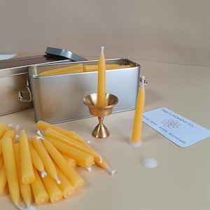 May include: A set of small yellow beeswax candles in a silver tin with a brass candle holder. The candles are arranged in a pile and there is a card that says "Take a moment to..." with a flower design.