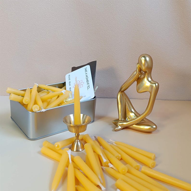 May include: A set of small, yellow beeswax candles in a silver tin with a brass candle holder. The candles are arranged in a pile and are ready to be lit. The text on the card reads "Take a moment to..."