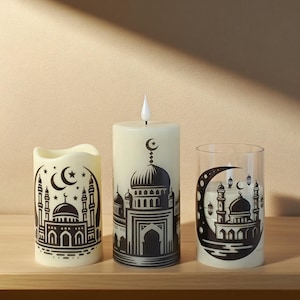 Könnte beinhalten: Drei dekorative Kerzen und ein Glaszylinder mit Moscheemotiven. Die Kerzen sind cremefarben mit schwarzen Moschee-Illustrationen, Monden und Sternen. Eine Kerze hat eine künstliche Flamme. Der Glaszylinder hat ein schwarzes Moscheemotiv in einem Mond.