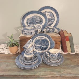 Puede incluir: Un juego completo de vajilla vintage azul y blanco. El juego incluye platos, cuencos, tazas, platillos, una fuente para servir y una jarra de crema. Cada pieza presenta un diseño de paisaje escénico con un borde detallado.