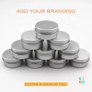 Puede incluir: Una pila de pequeños botes de aluminio plateado con tapas de rosca. El texto "ADD YOUR BRANDING" está en la parte superior y "CUSTOM ALUMINIUM TINS" en la inferior. Los botes están dispuestos en forma de pirámide.