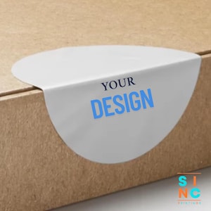 May include: A white, semi-circular sticker with the words "YOUR DESIGN" in blue text is adhered to a brown cardboard box. The sticker is partially wrapped around the edge of the box. The bottom right corner of the image shows the logo of a printing company.