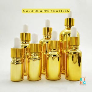 May include: A collection of gold dropper bottles with white droppers. The bottles vary in size and are arranged on a white background. The text "GOLD DROPPER BOTTLES" is displayed in a yellow rectangle.