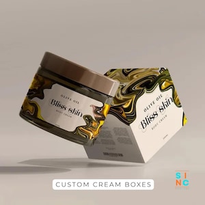 Puede incluir: Un tarro de cristal y una caja de crema corporal Bliss Skin. El tarro tiene una tapa marr&oacute;n y una etiqueta con el texto "Olive Oil Bliss Skin Body Cream". La caja tiene un dise&ntilde;o similar con el mismo texto y un patr&oacute;n de remolino amarillo y negro. El texto "Custom Cream Boxes" est&aacute; en la parte inferior.