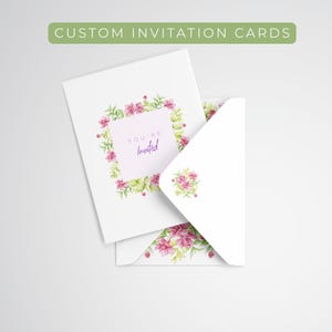 May include: White custom invitation cards with floral designs. The cards feature a square of pink flowers and green leaves, with the words "You're Invited" in a script font. The envelope has a matching floral design.