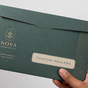 Puede incluir: Un sobre de correo personalizado de color verde oscuro con un logotipo dorado y el texto "NOVA PRINTING CO". El sobre tiene un patrón geométrico en el lado derecho y el texto "CUSTOM MAILERS" en una etiqueta.