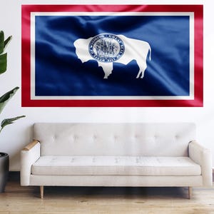 May include: A blue and red flag with a white buffalo and the words "Wyoming Great Seal" in a circle. The flag is hanging on a white wall.