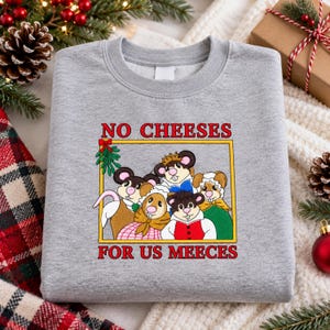 Könnte beinhalten: Ein graumeliertes Sweatshirt mit Rundhalsausschnitt und einem Grafikdruck von fünf Zeichentrickmäusen in einem gelben rechteckigen Rahmen. Der Text über und unter dem Rahmen lautet NO CHEESES FOR US MEECES in Rot. Die Mäuse tragen bunte Kleidung.