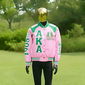 May include: Pink and green letterman jacket with the letters "AKA" on the front. The jacket has a green collar, shoulder accents, and trim. The number "1908" is on the left sleeve, and the word "green" is on the right sleeve.
