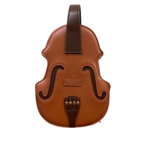 Puede incluir: Un bolso marrón con forma de violín con un asa y detalles en marrón oscuro. El bolso presenta un diseño detallado que imita un violín, incluyendo las efes y el puente. El bolso está hecho de un material liso y tiene cierre de cremallera.