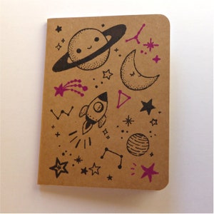 Recycled kraft notepad with celestial design of planets, stars, a space rocket, printed by hand.