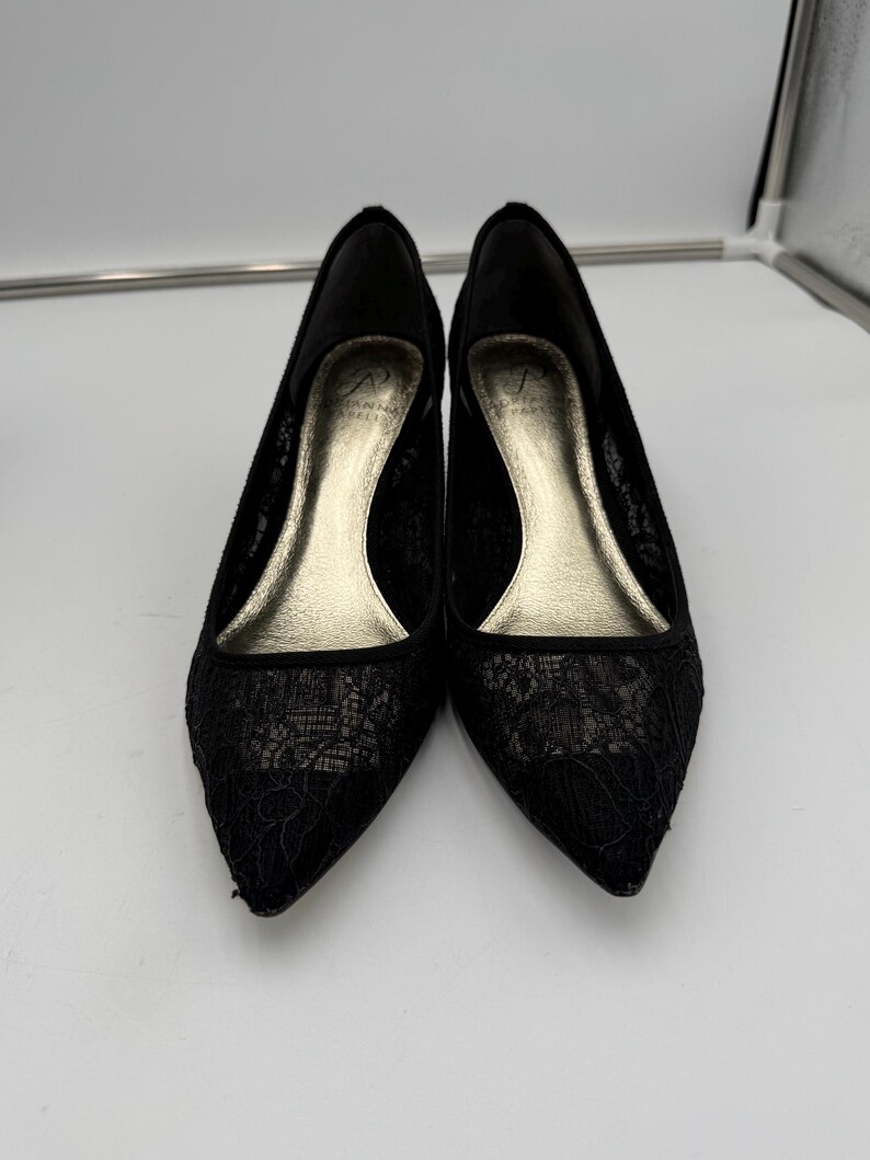 K&ouml;nnte beinhalten: Ein Paar schwarze Pumps mit Spitze und spitzer Zehenpartie. Die Innenseite der Schuhe ist goldfarben, die Abs&auml;tze sind niedrig. Die Schuhe stehen vor einem wei&szlig;en Hintergrund.