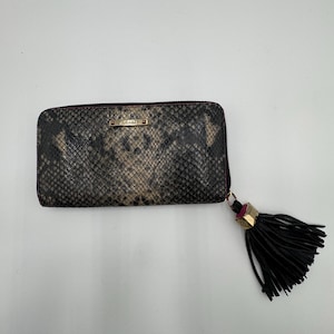 May include: A rectangular wallet with a snakeskin pattern in shades of gray and brown. The wallet has a zipper closure and a black tassel with gold accents. A small gold-colored plaque is visible on the front.