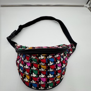 May include: A fanny pack featuring a colorful grid pattern of Mickey Mouse silhouettes in red, yellow, blue, green, and pink squares. The bag has a black zipper closure along the top and an adjustable black nylon strap with a plastic buckle.