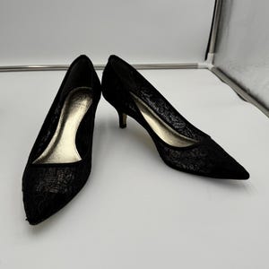 K&ouml;nnte beinhalten: Ein Paar schwarze Pumps mit Spitze, spitzer Zehenpartie und kleinen Abs&auml;tzen. Die Innenseite des Schuhs ist goldfarben. Die Schuhe stehen vor einem wei&szlig;en Hintergrund.