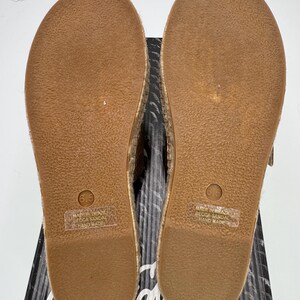 May include: Pair of espadrille sandals with a brown rubber sole, size 6.5. The sandals are handmade in Brazil. The soles are resting on a black and white patterned box.