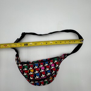 May include: A fanny pack featuring a repeating grid pattern of Mickey Mouse silhouettes in red, blue, yellow, and green squares. A black adjustable strap is attached. A yellow measuring tape shows the bag width is approximately 15 inches.