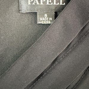 K&ouml;nnte beinhalten: Nahaufnahme eines schwarzen Kleidungsst&uuml;cks mit dem Etikett "ADRIANNA PAPELL". Das Etikett zeigt die Gr&ouml;&szlig;e 8 und "MADE IN CHINA". Der Stoff hat eine subtile Textur und diagonale Linien.