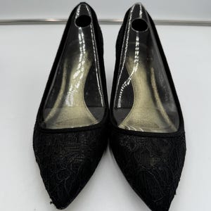 K&ouml;nnte beinhalten: Ein Paar schwarze Pumps mit spitzer Zehenpartie. Die Schuhe haben eine zarte Spitzenauflage auf der Zehenbox und den Seiten. Die Abs&auml;tze sind von moderater H&ouml;he, und die Innensohle ist durch ein transparentes Obermaterial aus Kunststoff sichtbar.